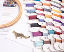 Colorful embroidery thread spools on a white surface with a wooden hoop and leopard pin.