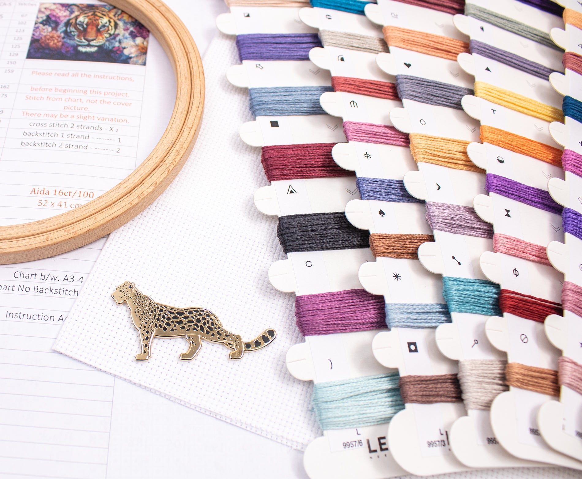 Colorful embroidery thread spools on a white surface with a wooden hoop and leopard pin.