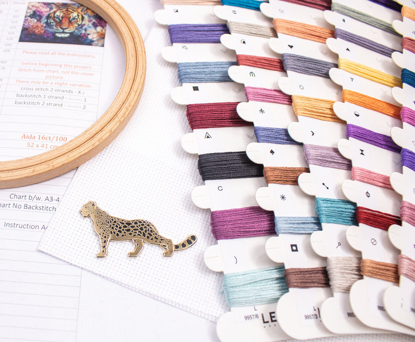 Colorful embroidery thread spools on a white surface with a wooden hoop and leopard pin.