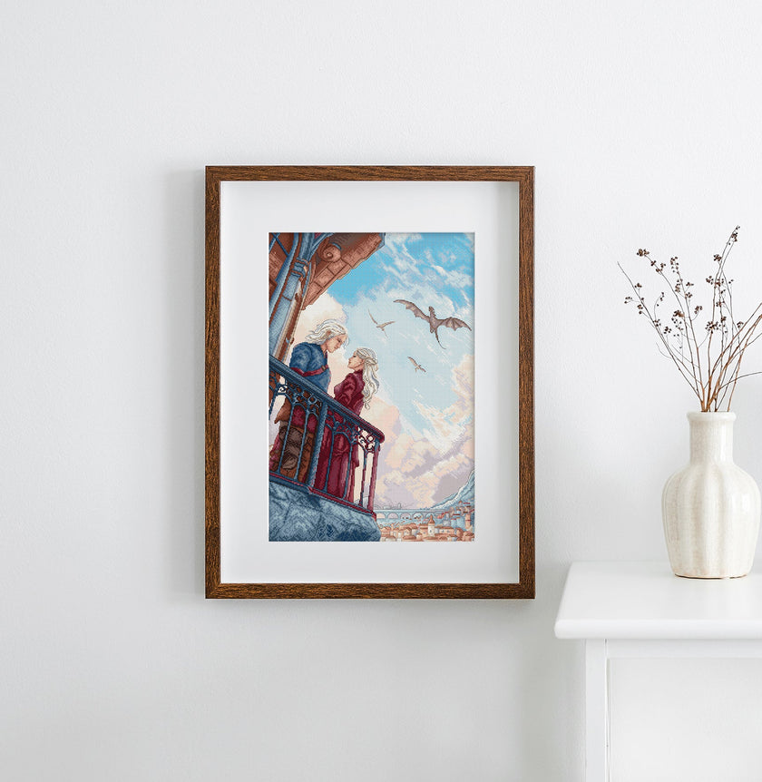 Framed artwork of a couple on a balcony with birds flying above, displayed on a wall next to a vase.