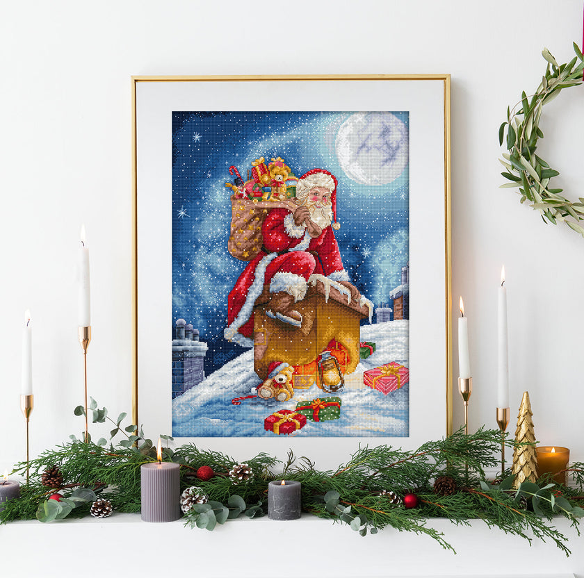 Framed artwork of Santa Claus on a sleigh with presents against a snowy night sky, displayed on a decorated Christmas mantel.
