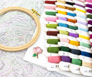 Embroidery hoop with cross-stitch pattern, colorful threads, and a pink rose pin on a white background.