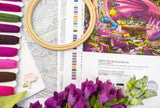 Embroidery hoop, fabric swatches, and floral elements on a table with a colorful embroidery design.