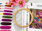 Embroidery hoop with colorful threads and a pattern book on a table.