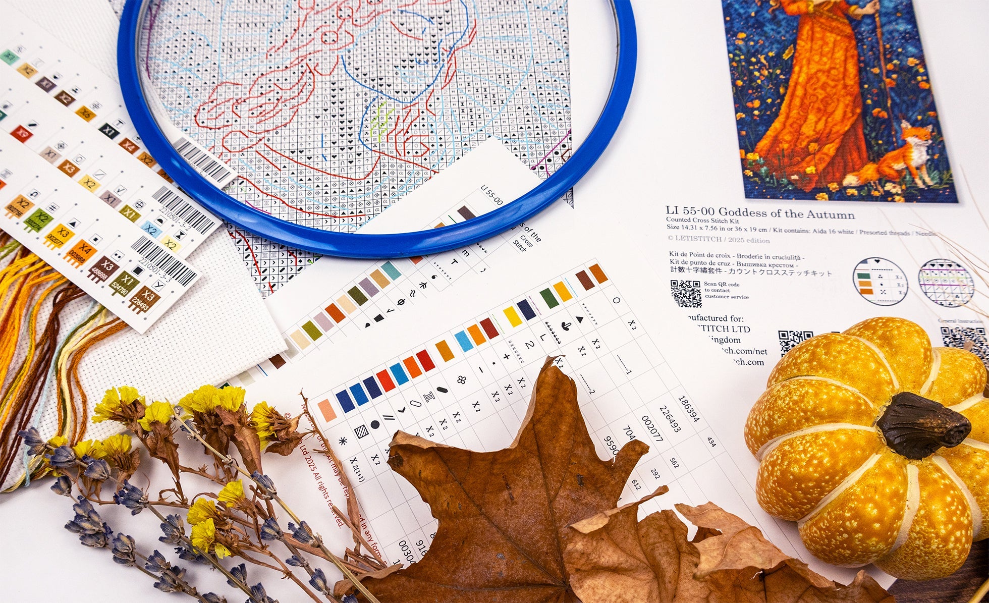 Embroidery hoop, fabric with pattern, color chart, and decorative items on a white surface