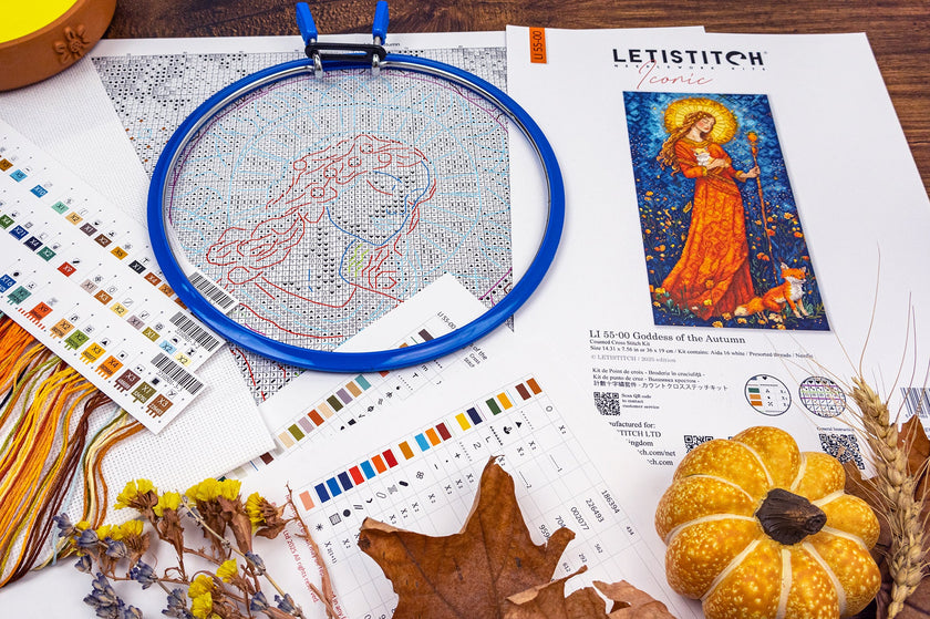 Cross-stitching materials with an embroidery hoop, pattern sheet, and decorative items on a wooden surface.