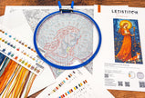 Embroidery hoop with cross-stitched design on a table with Letistitch embroidery kit and color swatches.