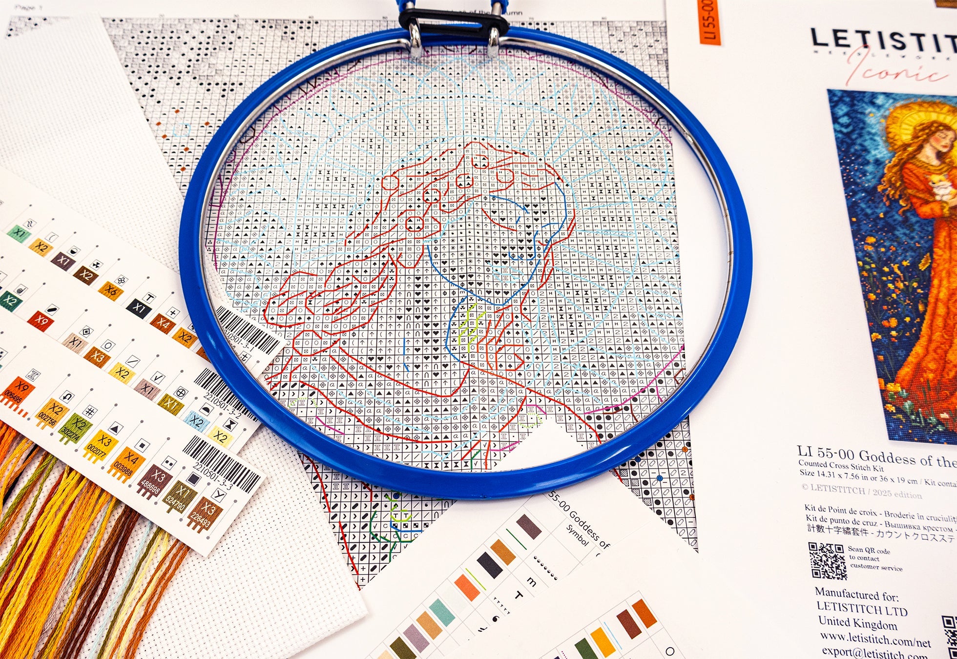 Embroidery hoop with cross-stitched design on a table with fabric and color swatches.