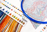 Embroidery hoop with cross-stitch pattern, color chart, and thread on a table.