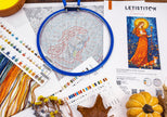 Cross-stitching hoop with fabric, threads, and pattern guide on a white surface