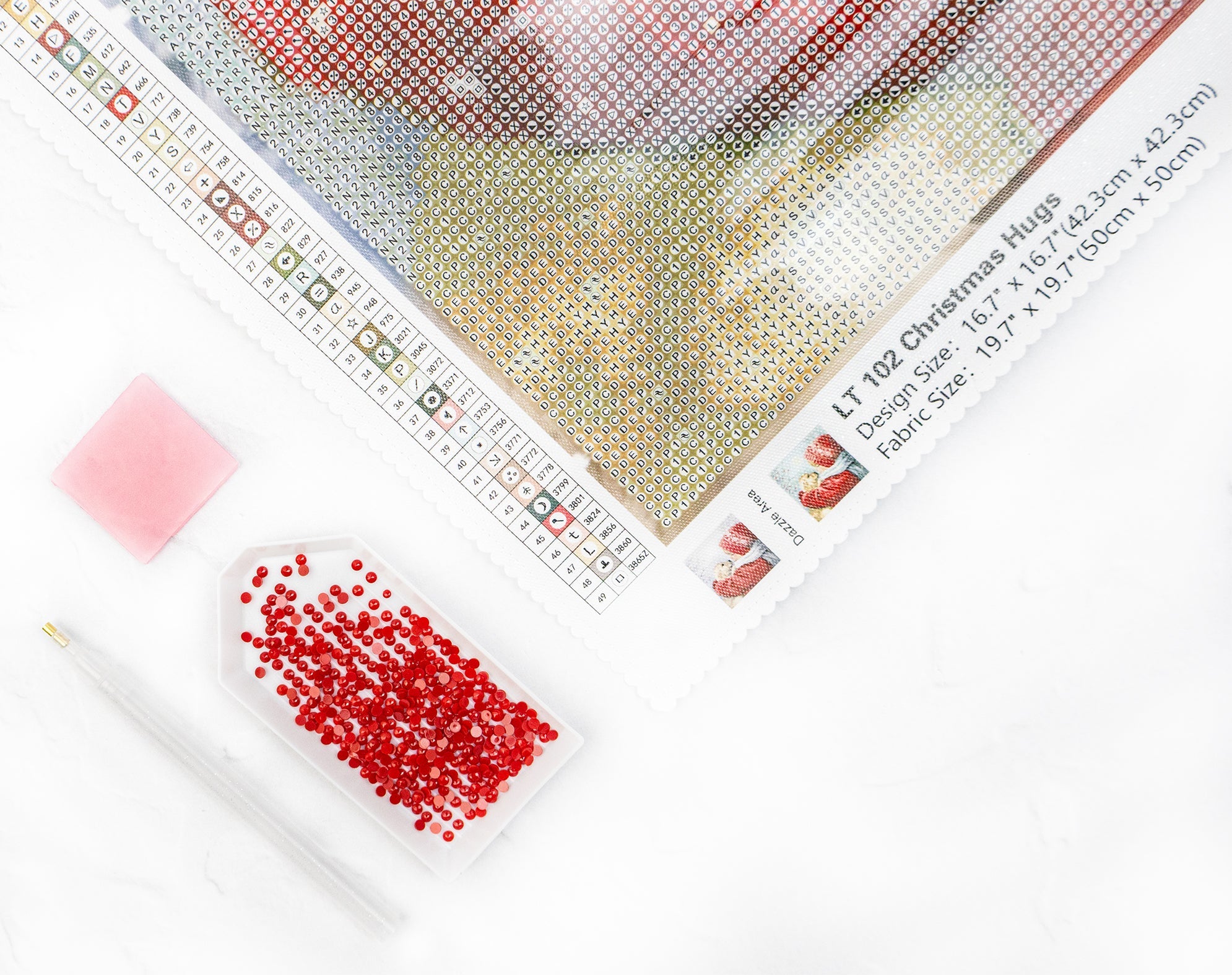 Cross-stitching kit with fabric, red beads, and a ruler on a white background
