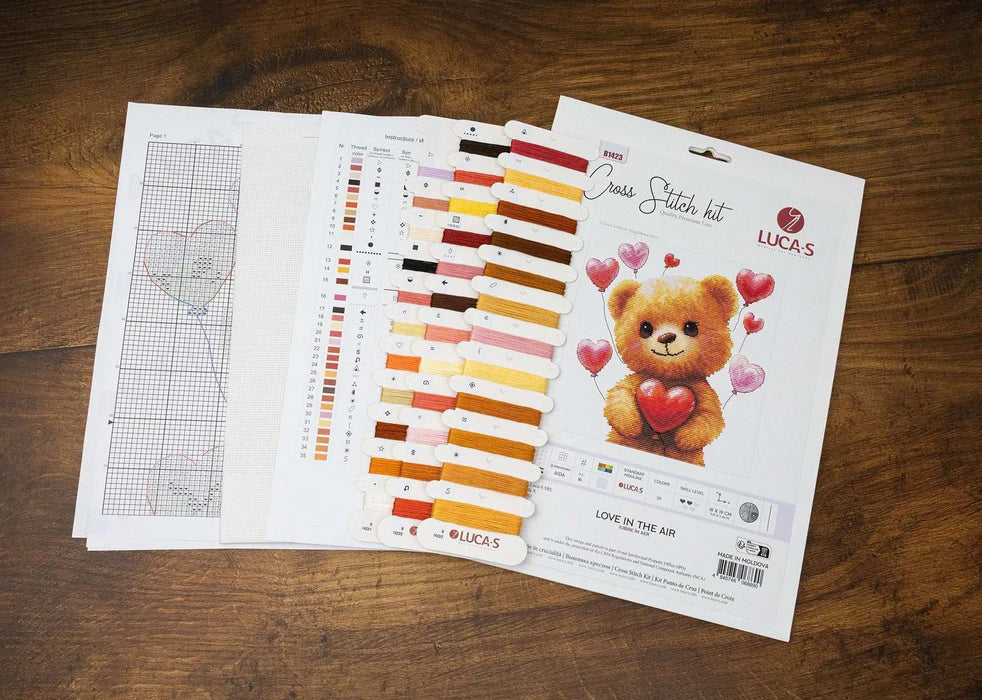 Cross-stitch kit with pattern, color chart, and teddy bear design on a wooden surface