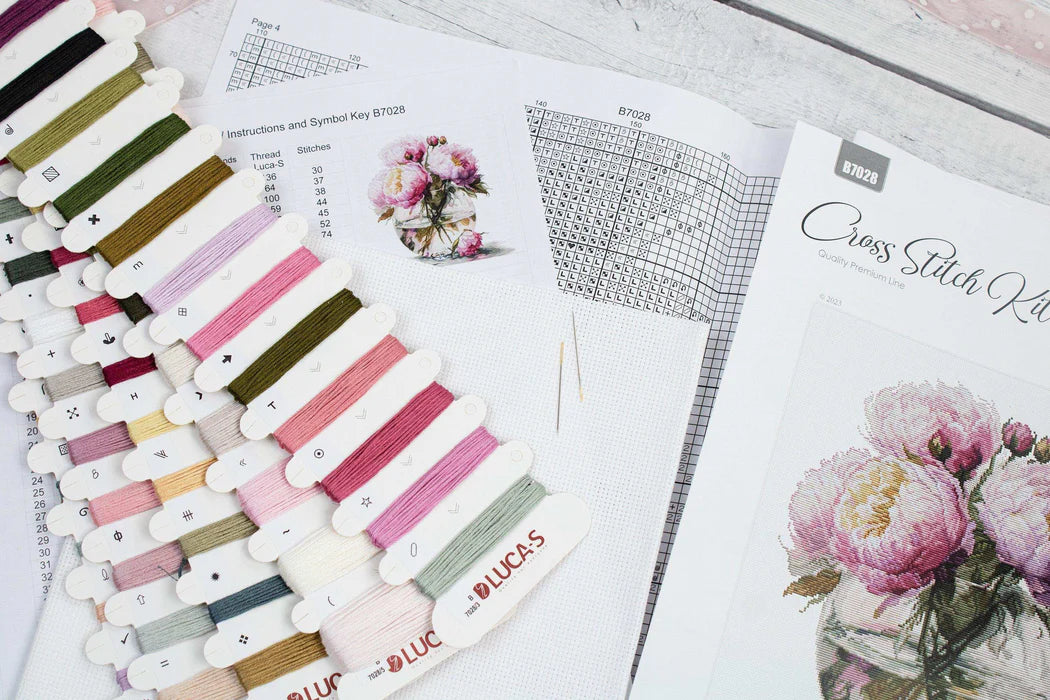 Set of embroidery thread spools and a cross stitch manual on a wooden surface