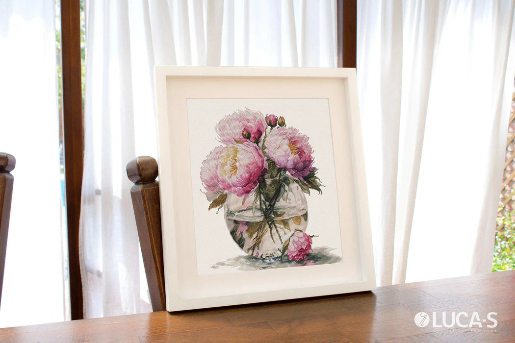 Framed artwork of a floral arrangement on a wooden table with white curtains in the background.