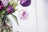 Floral cross-stitch pattern with purple and pink flowers in a glass jar on white fabric.