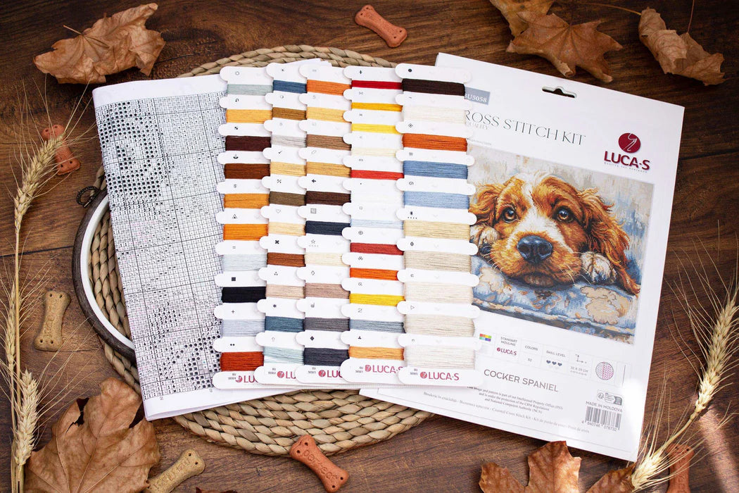 Cross stitch kit with thread colors and a dog illustration on a wooden surface with fall leaves.