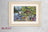 Framed cross-stitch artwork of a lakeside scene with animals and flowers, branded 'Lucas'.