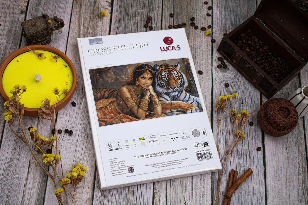 Cross-stitch kit packaging with a woman and tiger design on a wooden surface with decorative items.