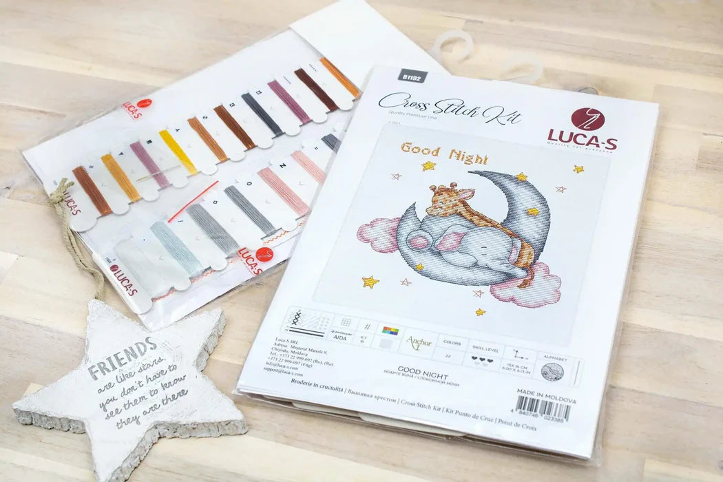 Cross stitch kit with a design of an elephant on a moon, surrounded by color swatches and branding.