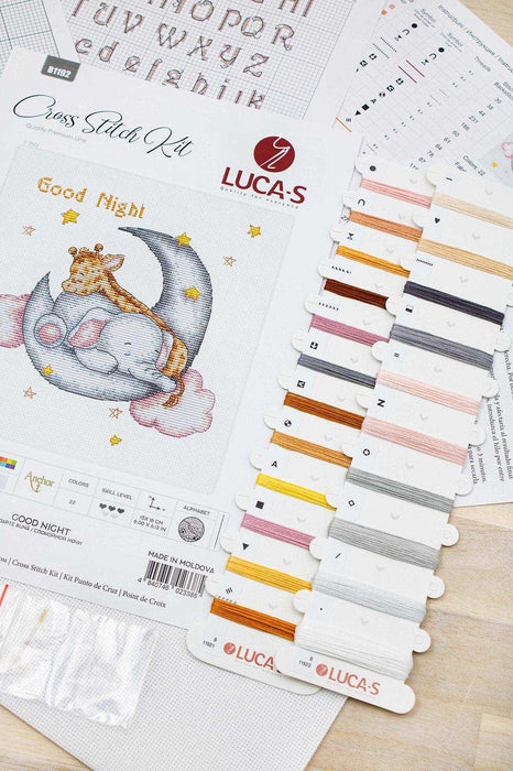Cross stitch kit with a design of a giraffe on a moon, accompanied by color swatches and threads.
