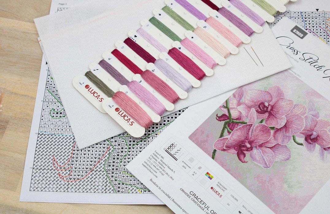 Cross stitch pattern with color swatches and floral design on a wooden surface