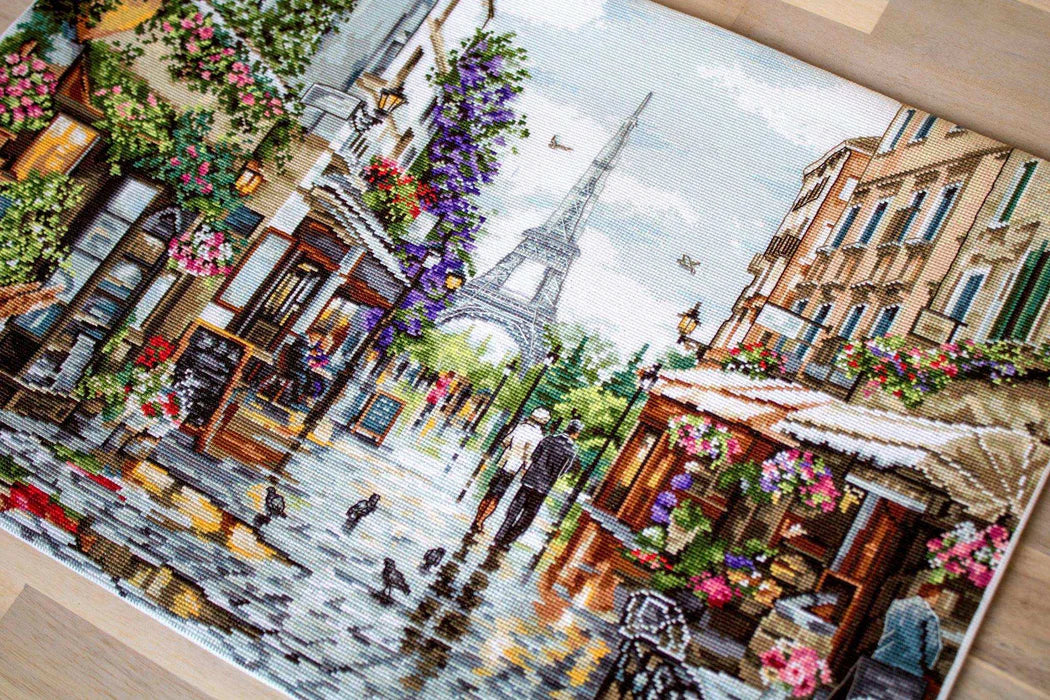 Cross-stitched city scene with Eiffel Tower and street vendors.