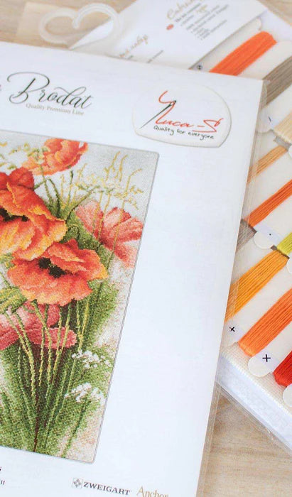 Cross-stitch pattern book with floral design and embroidery threads on a wooden surface