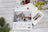 Lucas cross-stitch kit for 'Santa's Cottage' on a wooden surface with Christmas decorations.
