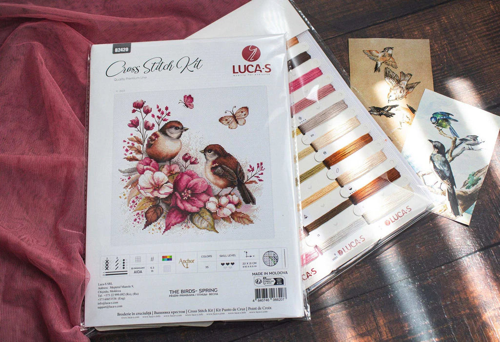 Lucas cross-stitch kit packaging with floral and bird design on a wooden surface.