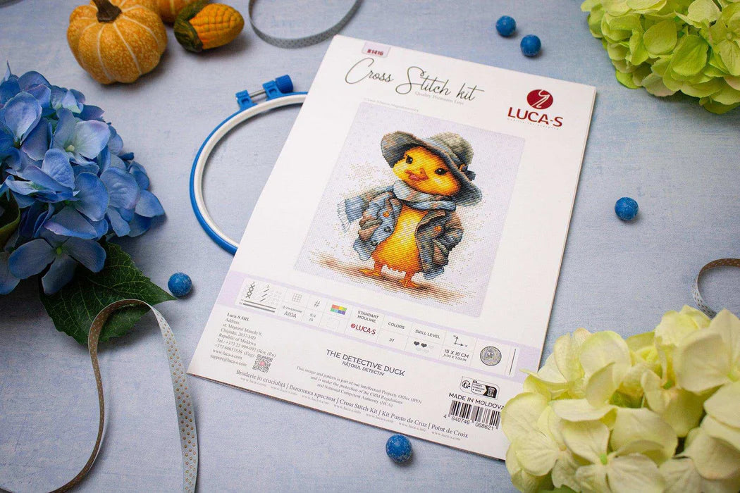 Cross stitch kit with a duck design on a table with flowers and embroidery hoop.