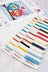 Colorful thread spools with 'LUCA' branding on a cross-stitching background